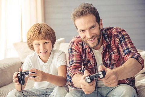 Cool full-bearded dad in a lumberjack shirt playing console games with his blond, enthusiastic six-year-old son