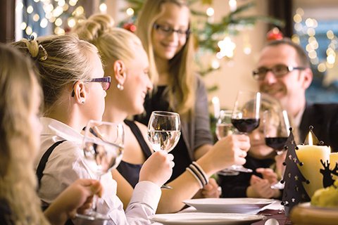 Festively dressed family at the beautifully decorated dining table, both parents toast with their ten-, thirteen- and sixteen-year-old blonde long-haired daughters