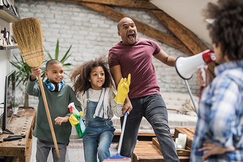 Familie mit Junge 10 Jahre und Mädchen 8 Jahre mit großem Spaß bei der Hausarbeit im Team, Mutter mit Megafon, Vater mit Wischer