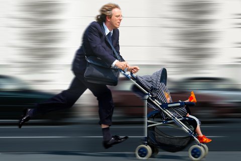 Berufstätiger Vater im Anzug rennt hektisch mit Kinderwagen 