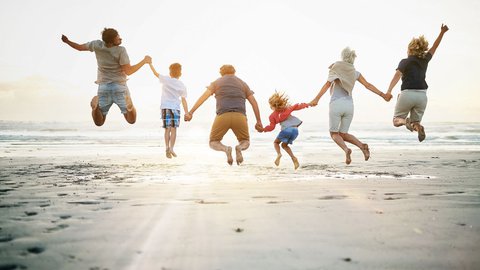 Großfamilie springt am Strand in der Abendsonne freudig in die Luft