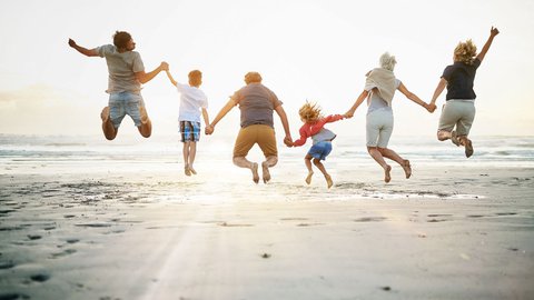 Großfamilie springt am Strand in der Abendsonne freudig in die Luft