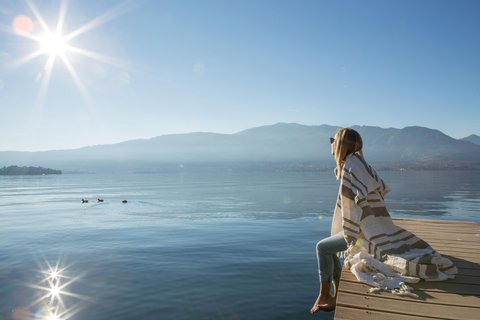 Erholte und glückliche junge Dame sitzt am Steg über dem See mit Bergpanorama